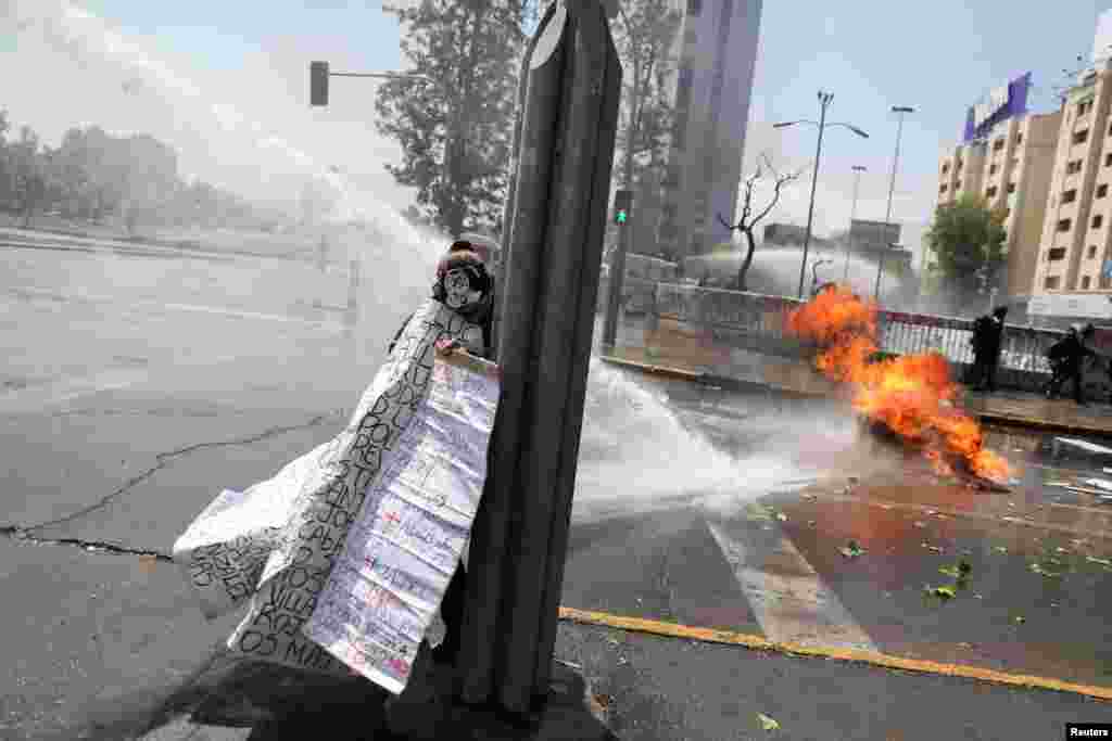 A person takes cover from a police water cannon as demonstrators take part in a rally on the third anniversary of the protests and riots that rocked the country in 2019, in Santiago, Chile.