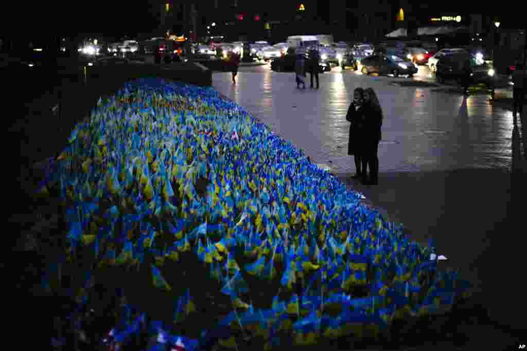 Two woman look at Ukrainian flags placed in memory of civilians killed during the war at the Independence square in central Kyiv.
