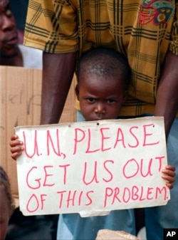 FILE - A Liberian child holds a sign pleading the United Nations to allow Liberians to leave the war-torn country of Liberia, while standing on the quay of Monrovia's port, May 17, 1996.