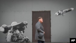 A man passes by graffiti depicting a Ukrainian soldier firing an anti-tank missile in Kyiv, Oct. 24, 2022. Writing on the missile reads: "The goal is one."