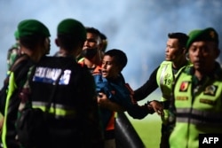 Seorang anak laki-laki (tengah) digendong anggota TNI mengamankan lapangan setelah pertandingan sepak bola antara Arema FC dan Persebaya Surabaya di Stadion Kanjuruhan di Malang, Jawa Timur (Foto: AFP)