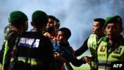 Seorang anak laki-laki (tengah) digendong oleh anggota TNI yang berusaha mengamankan satdion ketika kisruh berlangsung selepas pertandingan sepak bola antara Arema FC dan Persebaya Surabaya di Stadion Kanjuruhan di Malang, Jawa Timur, pada 1 Oktober 2022. (Foto: AFP)