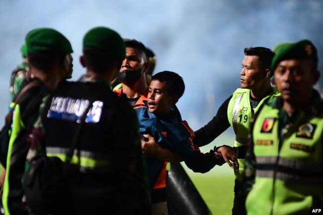 Seorang anak laki-laki (tengah) digendong anggota TNI mengamankan lapangan setelah pertandingan sepak bola antara Arema FC dan Persebaya Surabaya di Stadion Kanjuruhan di Malang, Jawa Timur (Foto: AFP)