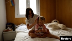 FILE - Ukrainian refugee Tatyana Bogkova brushes her daughter Eva's hair in the flat they share with other Ukrainian refugees in Madrid, Spain, Sept. 17, 2022. Bogkova, who left with her daughter and mother upon Russia's invasion of Ukraine, is struggling to find a job in Spain. 