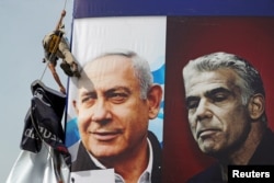 FILE - A laborer hangs a Likud party election campaign banner, depicting party leader Israeli Prime Minister Benjamin Netanyahu and his challenger, Yesh Atid party leader Yair Lapid, in Jerusalem, March 11, 2021.