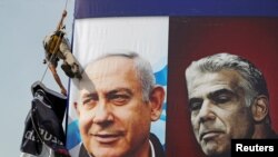 ARCHIVO - Un trabajador cuelga una pancarta de la campaña electoral del partido Likud, que representa al líder del partido, el primer ministro israelí, Benjamin Netanyahu, y su rival, el líder del partido Yesh Atid, Yair Lapid, en Jerusalén, el 11 de marzo de 2021.
