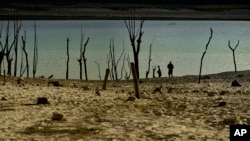 FILE - People walk close to the border at Yesa's reservoir affected by drought, in Yesa, northern Spain, Sept. 14, 2022. 