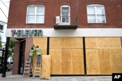 Workers board up the windows of a 7-Eleven convenience store in the Ybor City district in preparation for Hurricane Ian approaches the western side of the state, Sept. 27, 2022, in Tampa, Florida.