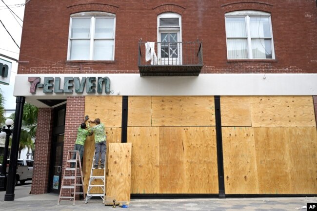 Workers board up the windows of a 7-Eleven convenience store in the Ybor City district in preparation for Hurricane Ian approaches the western side of the state, Sept. 27, 2022, in Tampa, Florida.