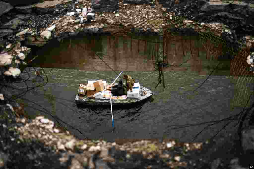 Yuri Shapovalov rows a boat full of goods as he and a Ukrainian serviceman cross the Siverskyi-Donets river under a destroyed bridge in Staryi-Saltiv, Ukraine. Shapovalov helps locals daily to cross the river with goods as the bridge was mostly destroyed during fighting.
