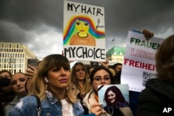 Women hold placards and photos of Iranian Mahsa Amini as they protest her death, in Berlin, Sept. 28, 2022.