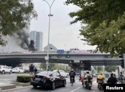 People watch while smoke rises as a banner with a protest message hangs off Sitong Bridge, Beijing, China October 13, 2022 in this image obtained by REUTERS.