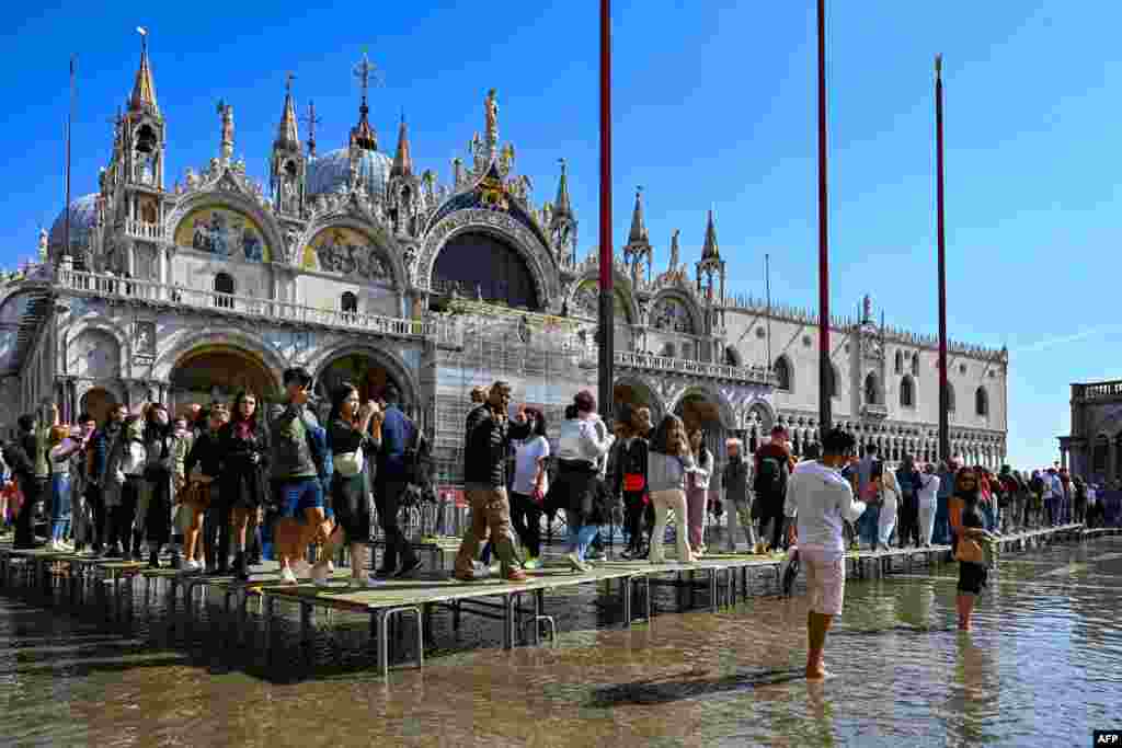 Tourists walk across elevated walkways outside St. Mark&#39;s Basilica on St. Mark&#39;s square in Venice, Italy.