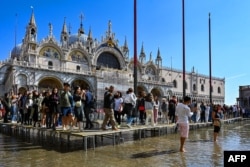FILE - Tourists walk across elevated walkways outside St. Mark's Basilica on St. Mark's square in Venice, Italy, Sept. 27, 2022. (Photo by ANDREA PATTARO / AFP)