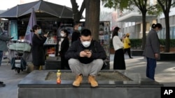 A man looks at his phone near a line for COVID tests in Beijing, Oct. 24, 2022. China's economic growth picked up in the latest quarter but still was among the weakest in decades as the ruling Communist Party tries to reverse an economic slump.