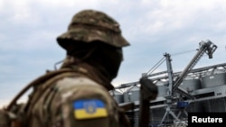 FILE - A Ukrainian serviceman stands in front of silos of grain at Odesa Black Sea port, in Odesa, Ukraine, July 29, 2022. On Oct. 29, Russia ended a U.N.-brokered deal allowing Ukraine to export grain by sea.