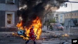 A medical worker runs past a burning car after a Russian attack in Kyiv, Ukraine, Oct. 10, 2022. Russia unleashed a lethal barrage of strikes against multiple Ukrainian cities Monday, smashing civilian targets.