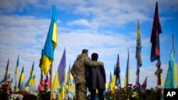 Parents of recently killed Ukrainian serviceman Ruslan Zhumaboev stand next to his grave in a cemetery during Ukraine Defenders Day in Kharkiv, Ukraine.