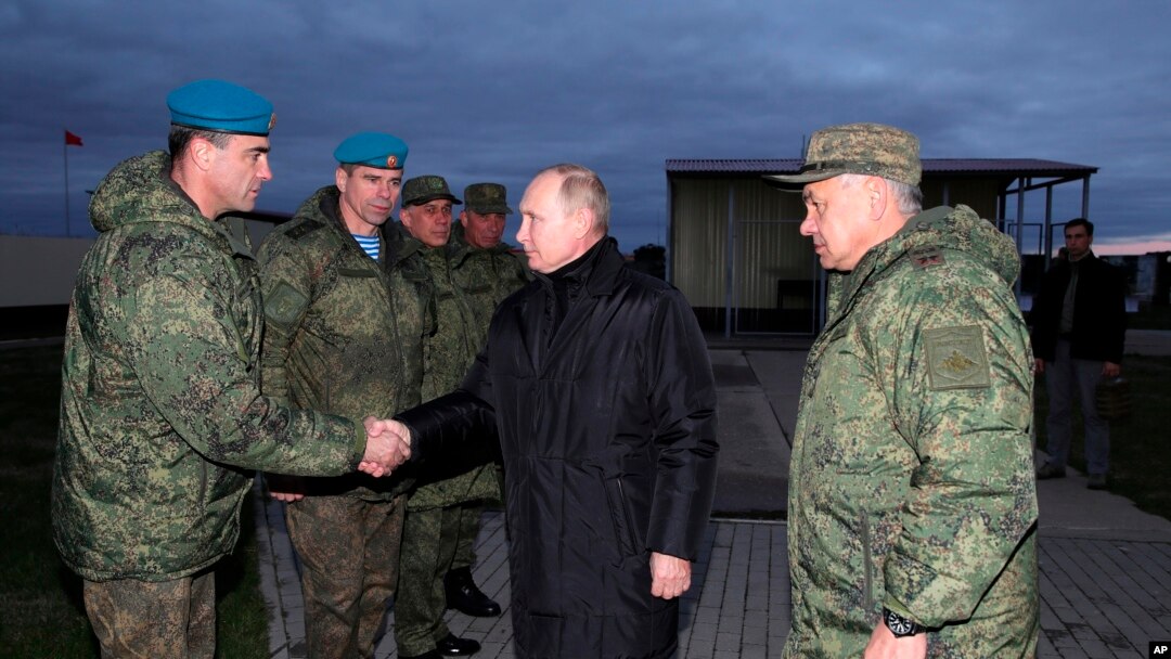 Russian President Vladimir Putin, center, greets Russian officers as he and Russian Defense Minister Sergei Shoigu, right, visit a military training center for mobilized reservists in Ryazan Region, Russia, Oct. 20, 2022.