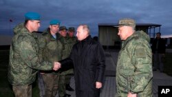 Russian President Vladimir Putin, center, greets Russian officers as he and Russian Defense Minister Sergei Shoigu, right, visit a military training center for mobilized reservists in Ryazan Region, Russia, Oct. 20, 2022.