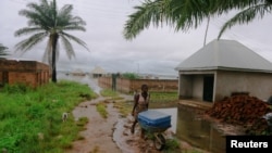 FILE - A lady pushes a wheel barrow as floodwater displaces residents living close to River Beune bank in Makurdi Nigeria, Oct. 1, 2022.