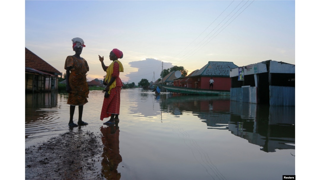 FILE - Two women wait for a canoe as floodwater overflows streets in Wadata in Makurdi, Nigeria, Oct. 1, 2022.