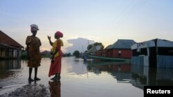 Dua perempuan tampak menunggu datangnya perahu ketika banjir menggenangi jalanan di Wadata, Makurdi, Nigeria, pada 1 Oktober 2022. (Foto: Reuters/Afolabi Sotunde)