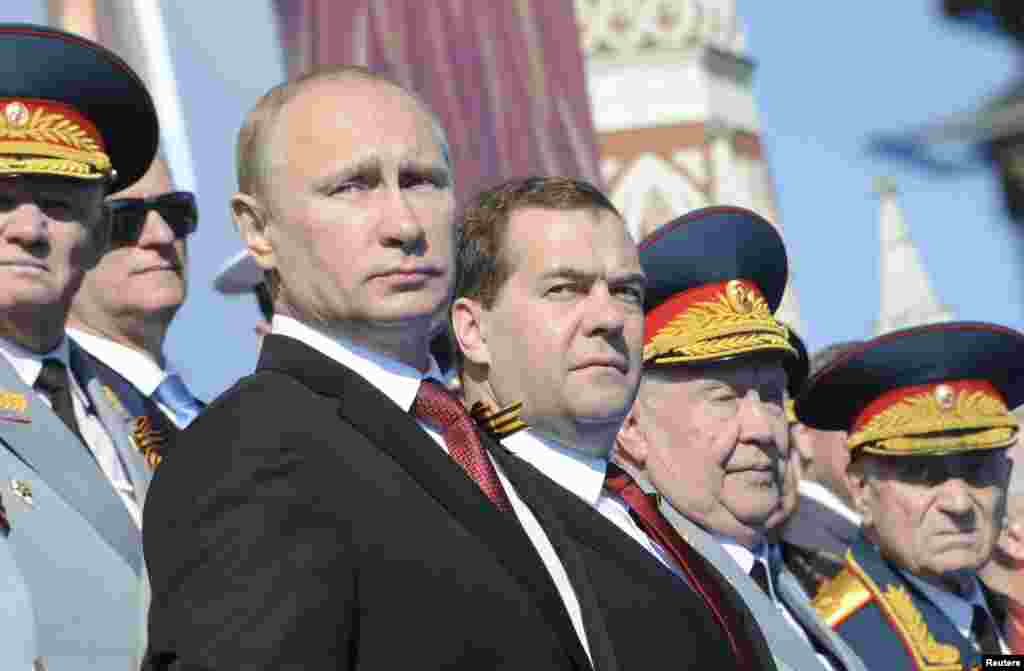 Presiden Rusia Vladimir Putin (depan kiri) dan PM Dmitry Medvedev (tengah) menyaksikan parade memperingati Hari Kemenangan Rusia dari podium di Lapangan Merah, Moskow.