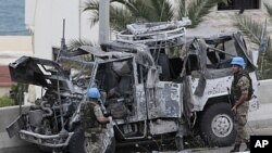 Two Italian UN peacekeepers stand guard next to a destroyed UN armored vehicle that attacked by a roadside bomb, in the southern port city of Sidon, Lebanon, May 27, 2011.