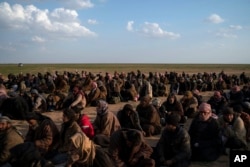 FILE - Men wait to be screened by U.S.-backed Syrian Democratic Forces (SDF) fighters after being evacuated out of the last territory held by Islamic State militants, near Baghuz, eastern Syria, Feb. 22, 2019.