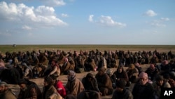 FILE - Men wait to be screened by U.S.-backed Syrian Democratic Forces (SDF) fighters after being evacuated out of the last territory held by Islamic State militants, near Baghuz, eastern Syria, Feb. 22, 2019.