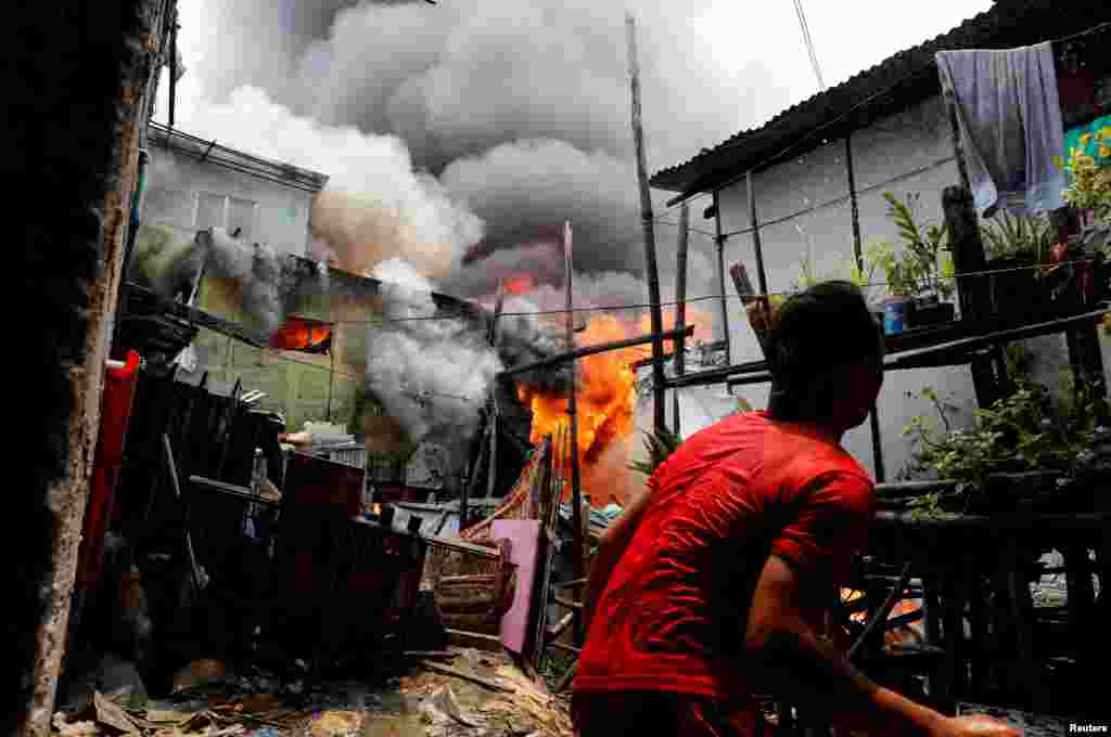 Seorang pria berusaha menyiramkan air ke arah rumahnya yang terbakar di kawasan permukiman informal Muntinlupa, Metro Manila, Filipina.