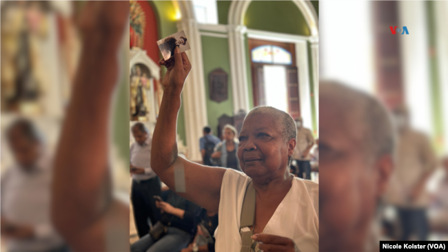 Una mujer que asegura que su hijo puede ver gracias a la intercesión de José Gregorio Hernández alza una estampa del beato.