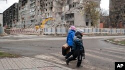 (FILE) Women walk past damaged apartment buildings in Mariupol, Ukraine. 