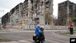 Gratë ecin përpara godinave të apartamenteve të shkatërruara në Mariupol (4 nëntor 2022)