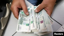 FILE - An employee counts Russian ruble bank notes at a private company's office in Krasnoyarsk, Siberia, Dec. 17, 2014. Sanctions linked to the Ukraine crisis could end up costing Russia 9 percent of its gross domestic product, says International Monetary Fund.