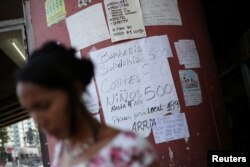 A woman walks past placards with prices of different products and services in a street of Caracas, Venezuela, Jan. 28, 2019.