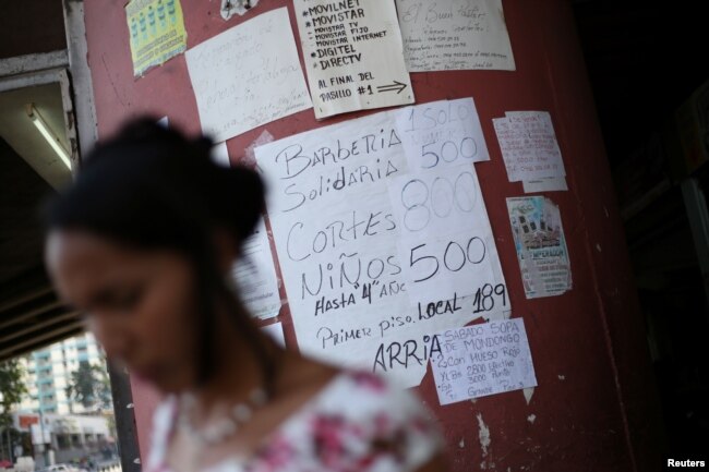 A woman walks past placards with prices of different products and services in a street of Caracas, Venezuela, Jan. 28, 2019.