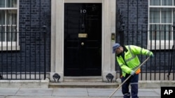 A workman sweeps up leaves in front of 10 Downing Street in London, Oct. 30, 2019. 
