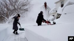 Susan Iannuzzi, left, and Linda Marzell clear a sidewalk after a heavy snowfall on street in Binghamton, New York.