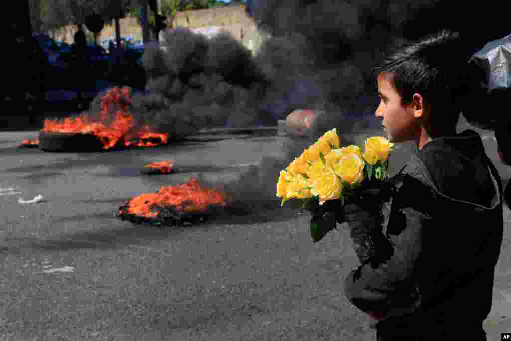 레바논 베이루트에서 물가 상승과 화폐가치 하락에 항의하는 시위대가 타이어를 불태우자 꽃을 파는 소년이 바라보고 있다.