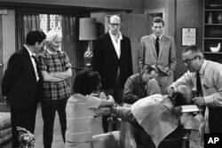 FILE- In this April 11, 1963, file photo, standing from left, Morey Amsterdam, Rose Marie, and Richard Deacon, and Dick Van Dyke, right, gather around Carl Reiner, in barber chair during a rehearsal of an episode for the "The Dick Van Dyke Show."