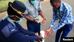 Un officier de police montre à un visiteur comment désinfecter ses mains contre la propagation du coronavirus à Harare au Zimbabwe, le 19 mars 2020.