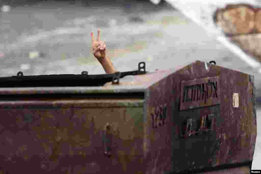 A Palestinian protester gestures as he hides behind a metal container during clashes with Israeli security forces in east Jerusalem, Oct. 30, 2014. 