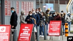 Customers stand in line for picking up online orders at an electronic market in Essen, Germany, during the lockdown due to the COVID-19 pandemic on Tuesday, Feb. 2, 2021.