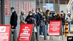 Customers stand in line for picking up online orders at an electronic market in Essen, Germany, during the lockdown due to the COVID-19 pandemic on Tuesday, Feb. 2, 2021.