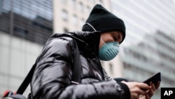 In this file photo, a pedestrian uses her phone while wearing a face mask in Herald Square, Thursday, March 12, 2020, in New York. (AP Photo/John Minchillo)
