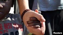 El inmigrante malí Kouyate Fatoumata, de 4 años, camina de la mano del activista Arce García, de 27, de Barcelona, España, antes de desembarcar en el puerto de Trapani, Italia, el sábado, 19 de agosto de 2017.