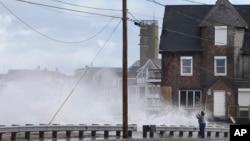 A woman takes pictures of the high surf, March 6, 2018, as waves continue to breach the seawall in Marshfield, Massachusetts. 