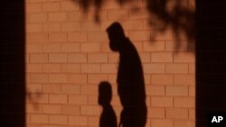 FILE - The shadow of an adult and a child is cast on the wall as they walk to a classroom in Davie, Fla., Oct. 9, 2020. (AP) 